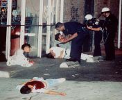 Police officers questioned three injured Koreans near the Korean-owned pizza parlor in Los Angeles, while the fourth Korean, seen in the foreground, laid dead in his bloodied shirt after being shot while trying to protect the parlor during the 1992 Los An from latifndian parlor